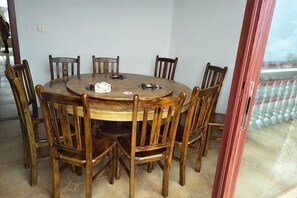 A round wooden dining table with chairs, a glass door, and a view of a balcony.