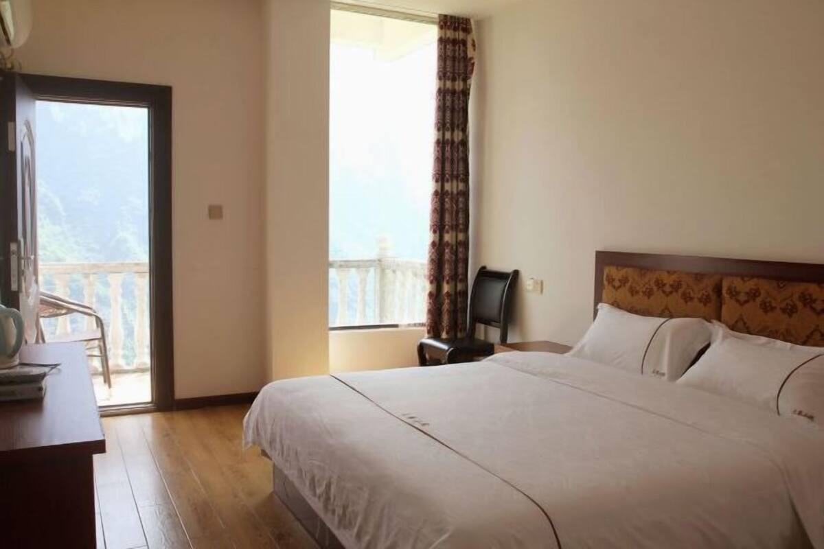 Habitación de hotel con cama, escritorio, silla, ventana con cortinas y balcón.
