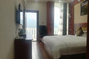 Ein Schlafzimmer mit einem Bett, einem Fernseher auf einem Schrank, einer hölzernen Kommode und einem Balkon mit Blick.