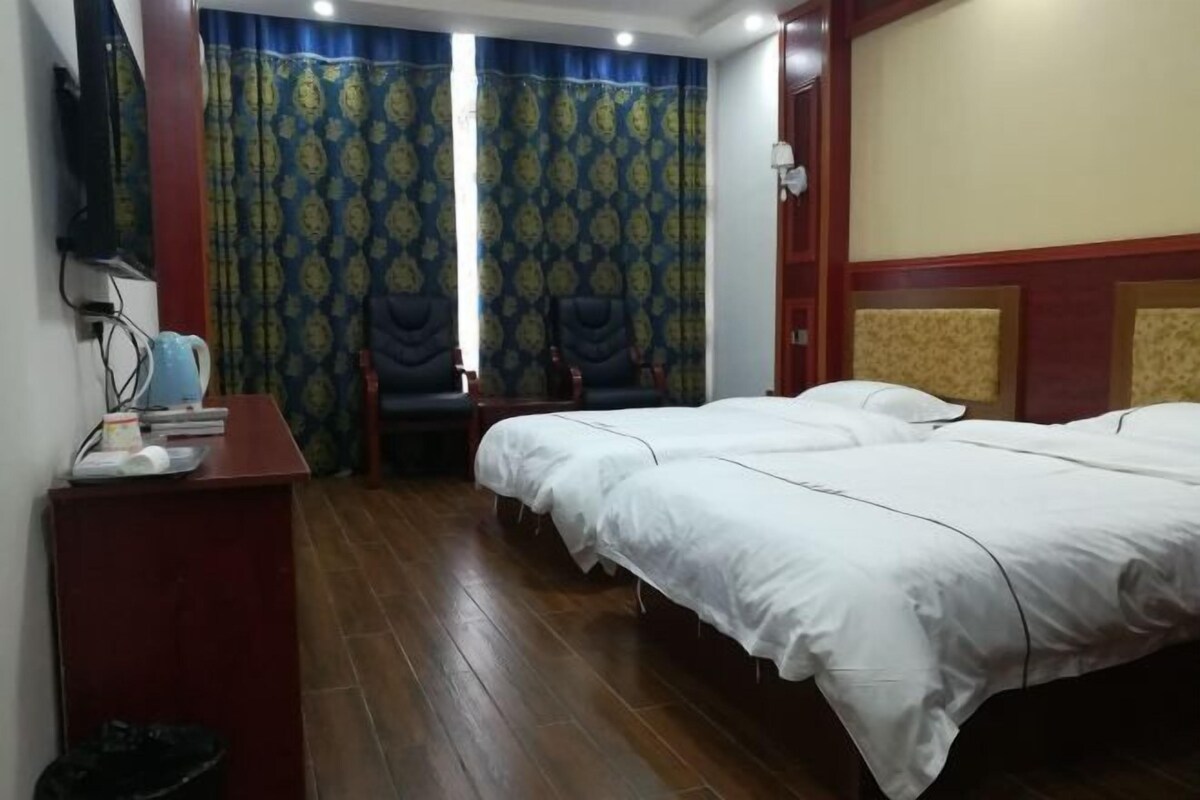 Ein Hotelzimmer mit zwei Betten, einem Schreibtisch mit Stuhl, einem Fernseher und einem Vorhang mit Muster.
