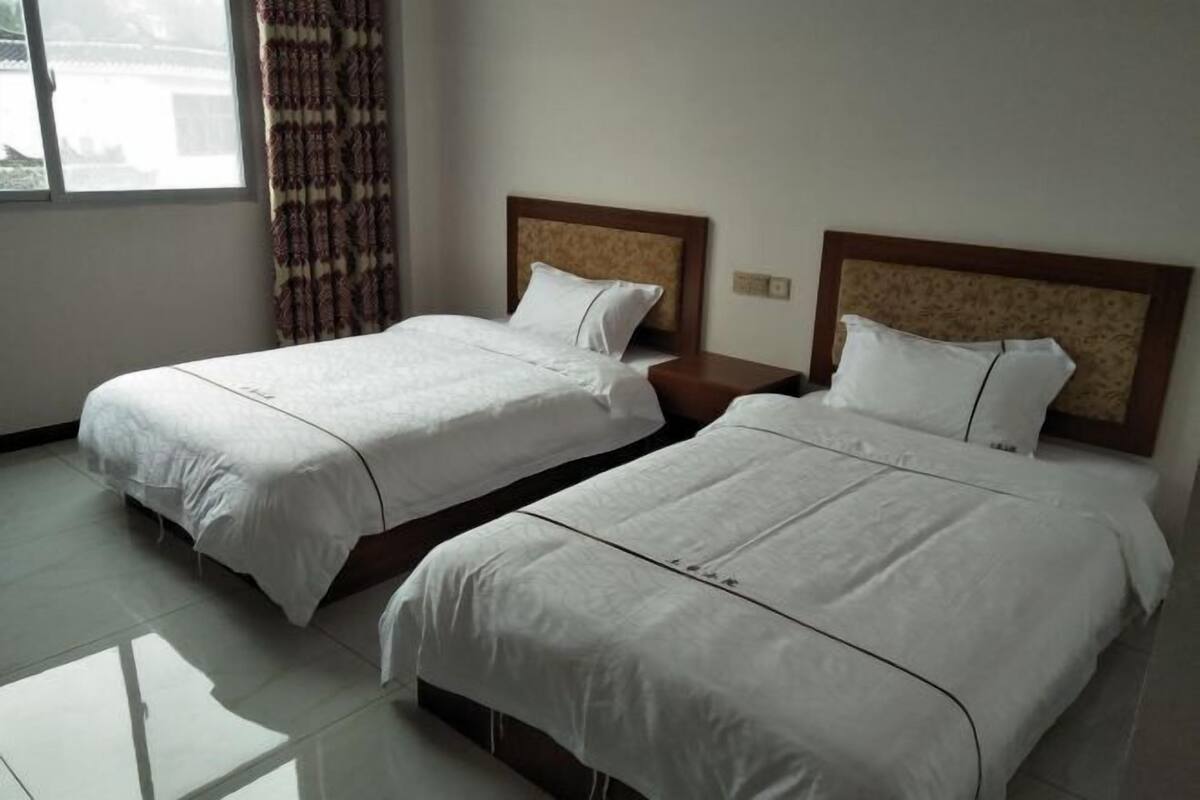 Dos camas individuales con cabeceros de madera, una ventana con cortinas y un piso de baldosas.