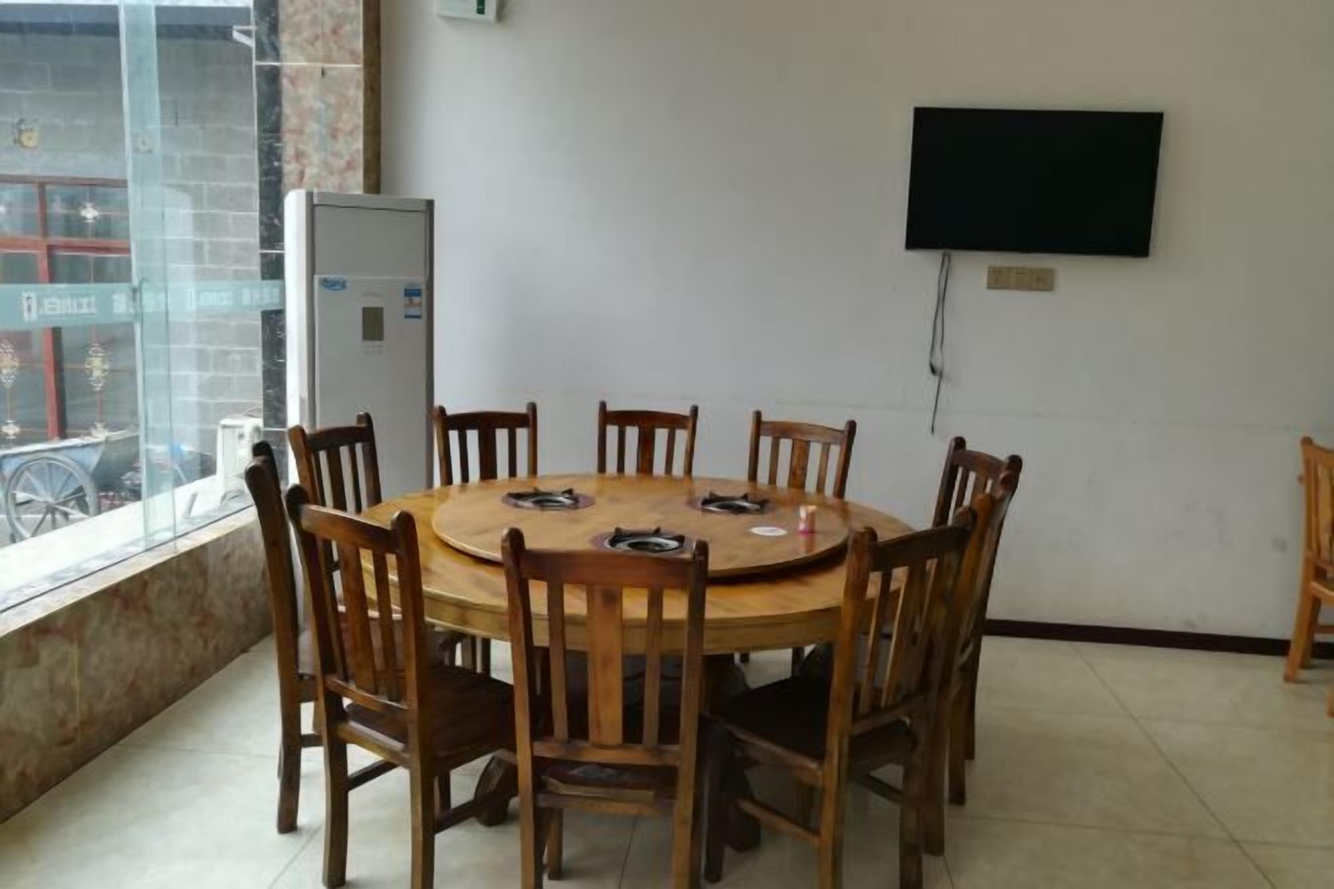 A conference room with a round wooden table and chairs, a flat-screen TV mounted on the wall, and a window with a view of the outside.