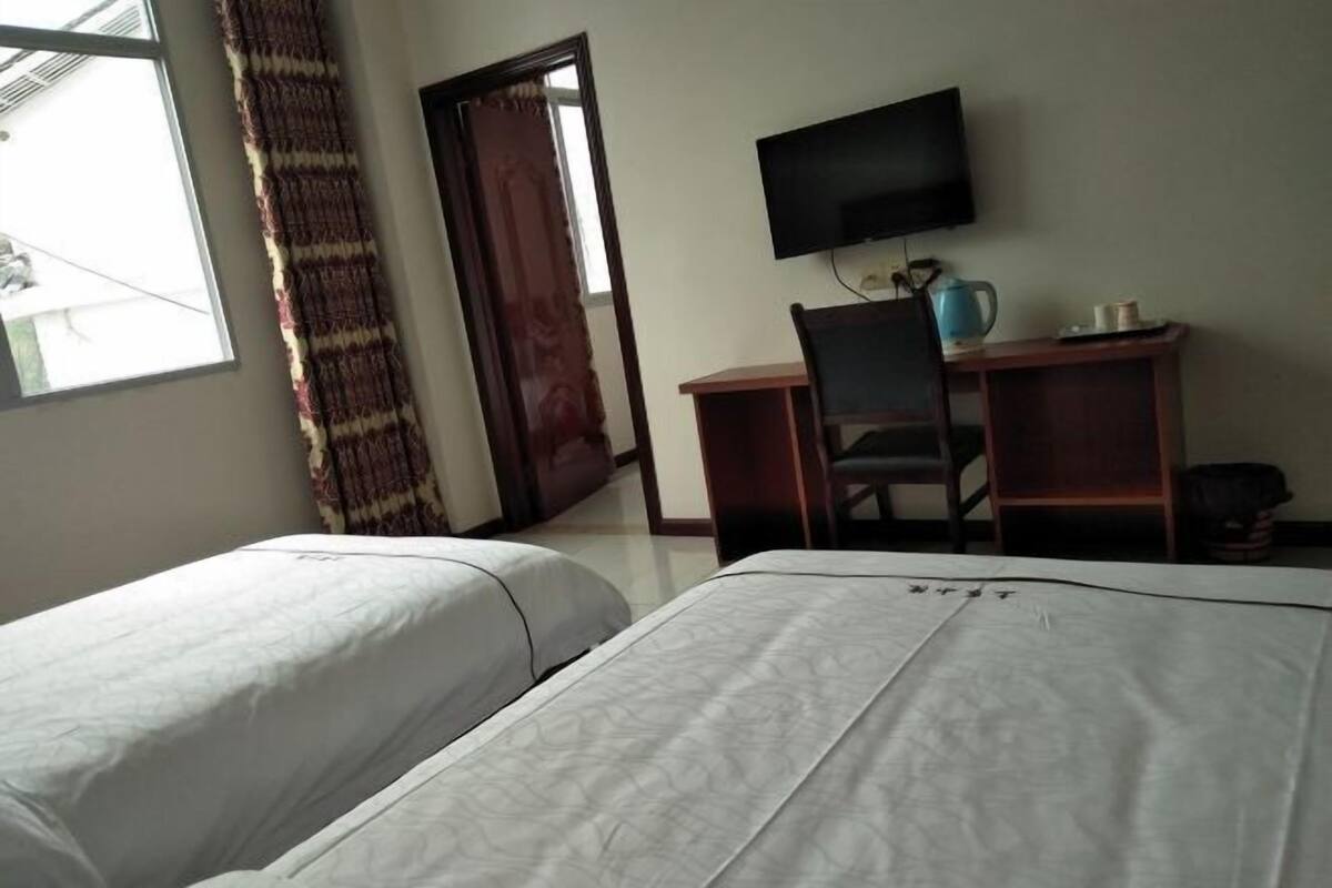 Habitación de hotel con dos camas, un escritorio con silla, televisión y ventana con cortinas.