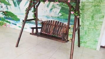 A wooden swing set with a bench, decorated with pink flowers, against a backdrop of a waterfall mural.
