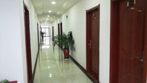 A long, narrow hallway with a shiny tiled floor, wooden doors on both sides, and a potted plant in the center.
