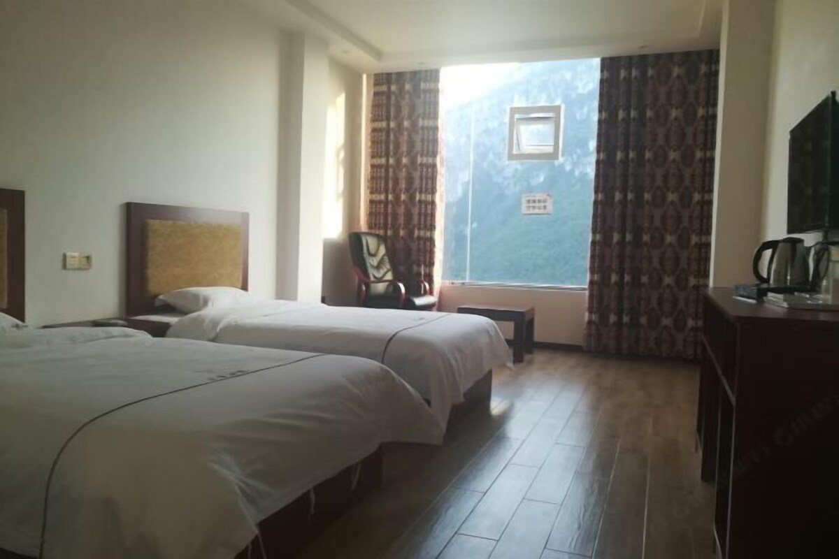 Ein Hotelzimmer mit zwei Betten, einem kleinen Tisch, einem Sessel und einem Fenster mit Vorhängen.