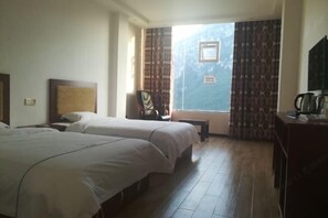 Ein Hotelzimmer mit zwei Betten, einem kleinen Tisch, einem Sessel und einem Fenster mit Vorhängen.