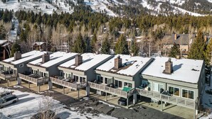 Un edificio moderno con varios balcones, rodeado de montañas nevadas y bosques densos.