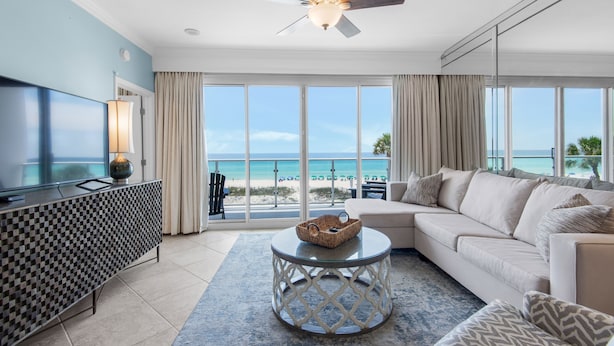 A modern living room with a large TV, a ceiling fan, and a view of the beach.