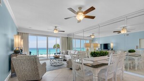 A spacious living area with a dining set, ceiling fans, and a large window overlooking the ocean.