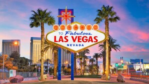The iconic Las Vegas sign with palm trees and cityscape in the background.