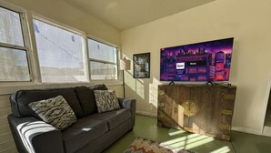 A living room with a gray sofa, patterned cushions, a colorful rug, a wooden cabinet, and a large TV on the wall. - 4BR, 2-house compound close to UA, Downtown Tucson (Tucson)