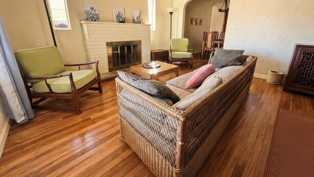 A cozy living room with a wicker sofa, a green armchair, and a wooden coffee table. A fireplace is visible in the background. - 4BR, 2-house compound close to UA, Downtown Tucson (Tucson)
