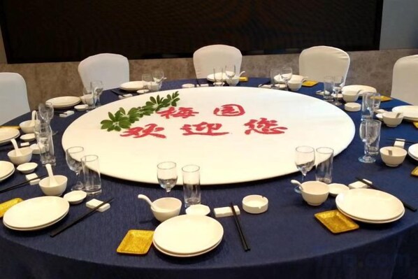 Una mesa redonda dispuesta para un evento formal, con un mantel individual central que muestra texto, rodeada de sillas y cubiertos.
