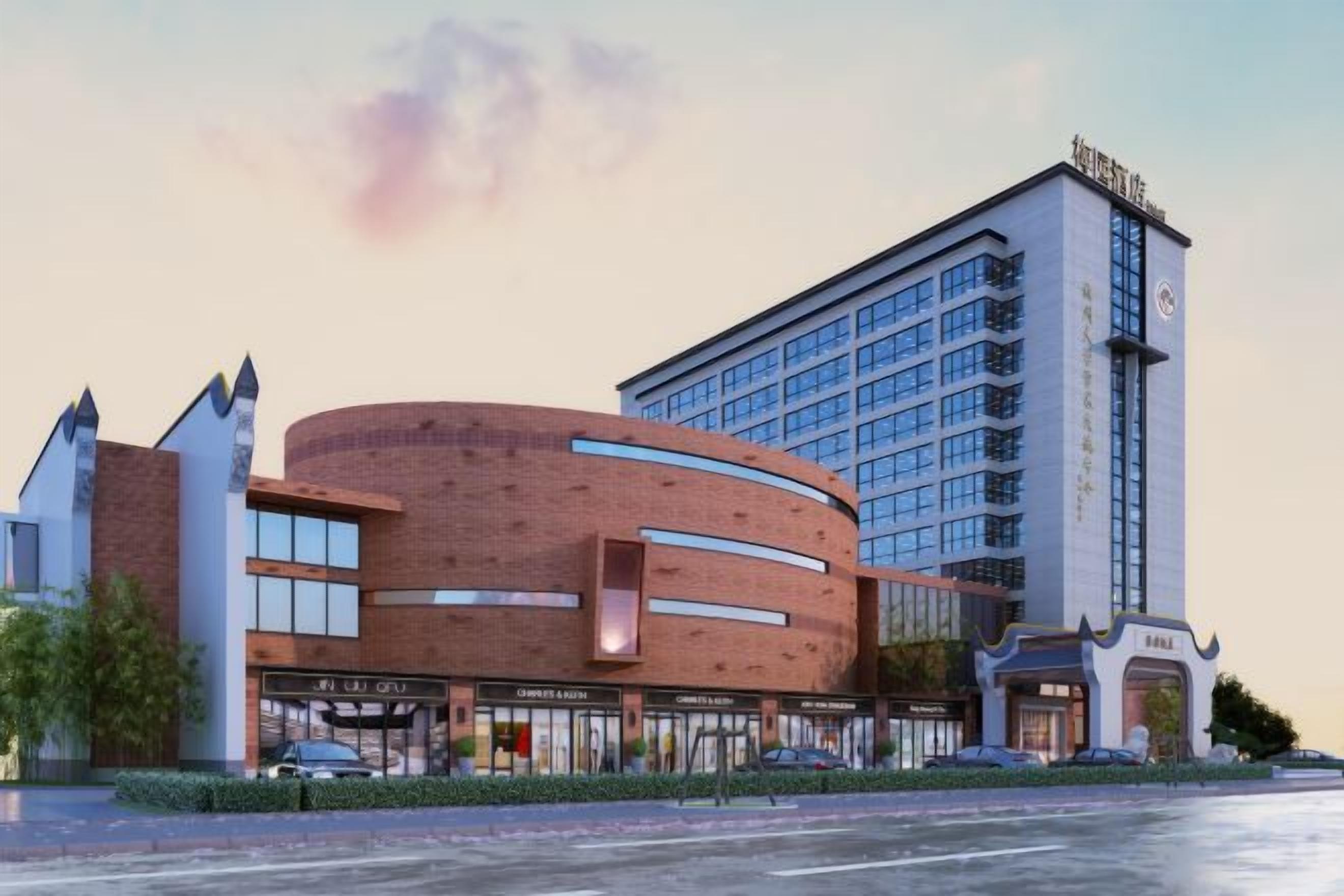 A modern hotel with a curved brick facade, a tall adjacent building, and a well-maintained parking area.
