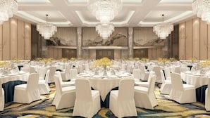 Une salle de banquet avec des tables rondes, des chaises blanches, des lustres et un sol recouvert de moquette.