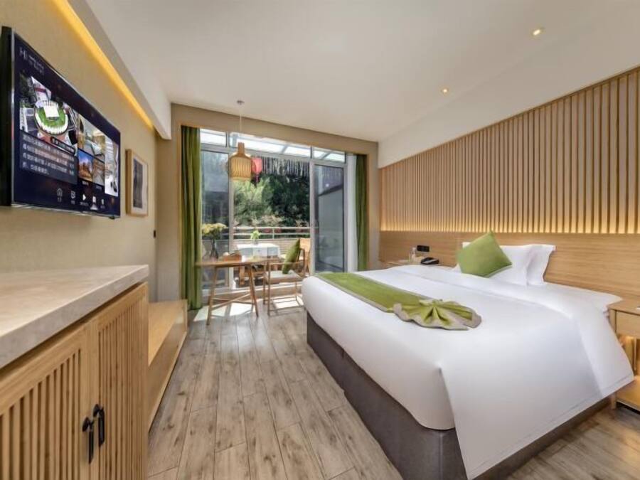 Ett modernt hotellrum med en stor säng, ett träfärgat sänggavel, ett skrivbord med en stol och utsikt över grönområden genom fönstret.