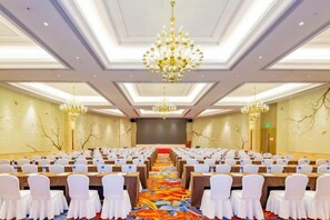A conference room with rows of white chairs, a long table at the front, and chandeliers. - Yishan Meiyuan Hotel (Fuzhou)