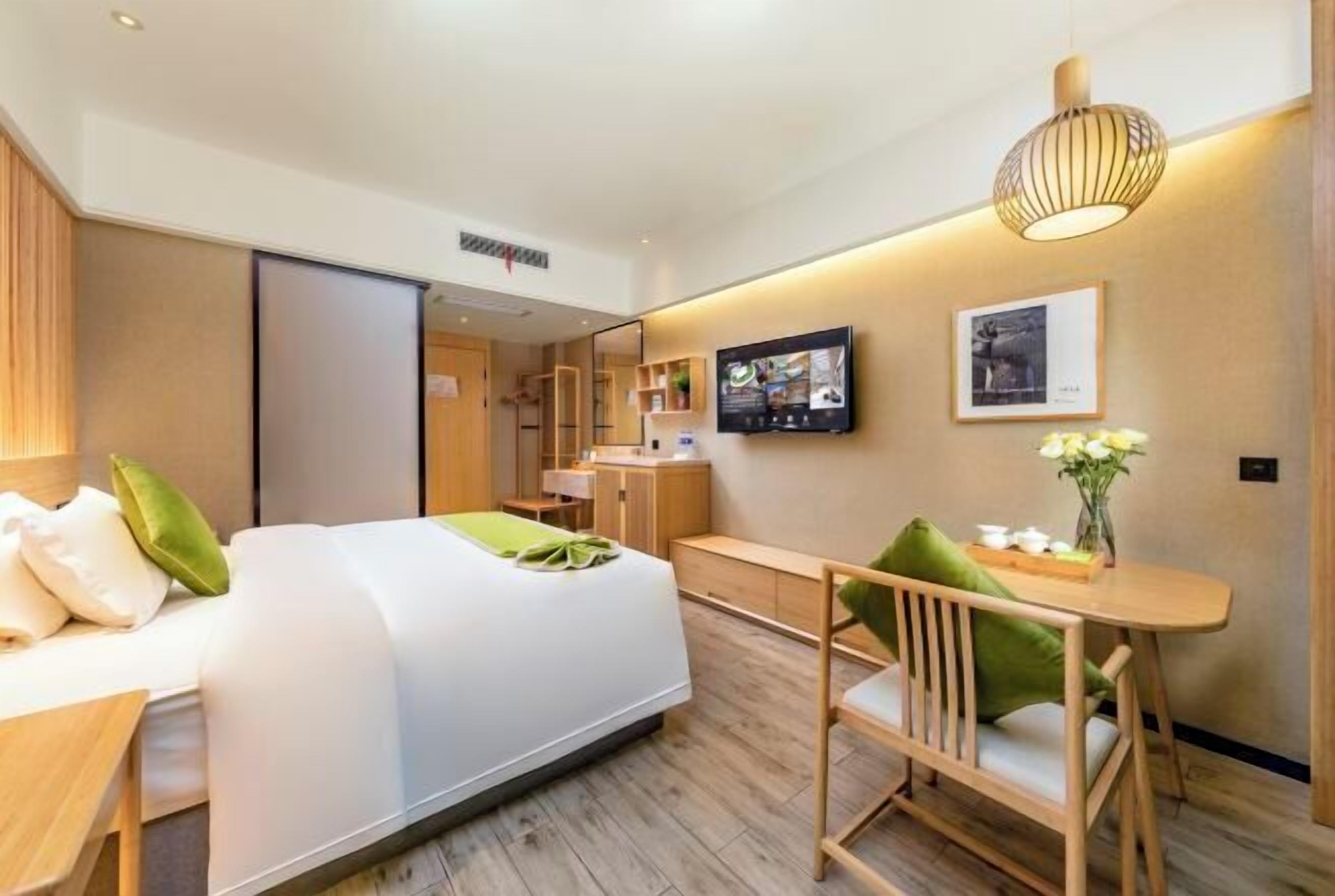 Una habitación de hotel moderna con cama, escritorio, silla, televisor y una pequeña mesa con flores.