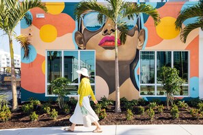 Un edificio con un mural colorido, palmeras y una vereda para peatones.
