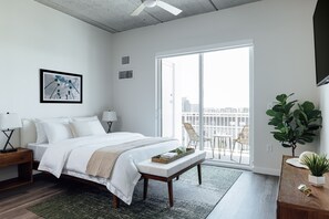 A modern bedroom with a large bed, bedside tables, a bench, a potted plant, and a view of the city through a sliding glass door. - Mint House St. Petersburg Downtown by Kasa (St. Petersburg)