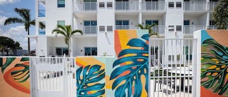 A multi-story hotel with balconies, palm trees, and a gated entrance with colorful artwork.