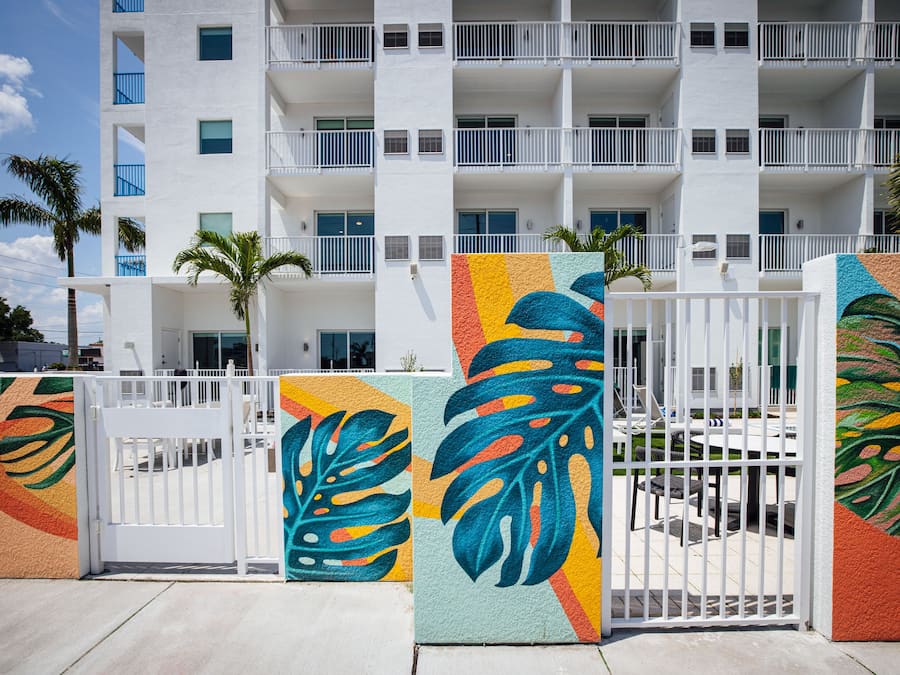 Un hotel de varios pisos con balcones, palmeras y una entrada porticada con coloridas obras de arte.