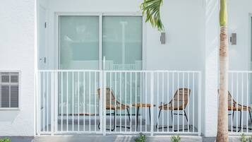 A white building with a balcony, two wicker chairs, a palm tree, and a small garden area.