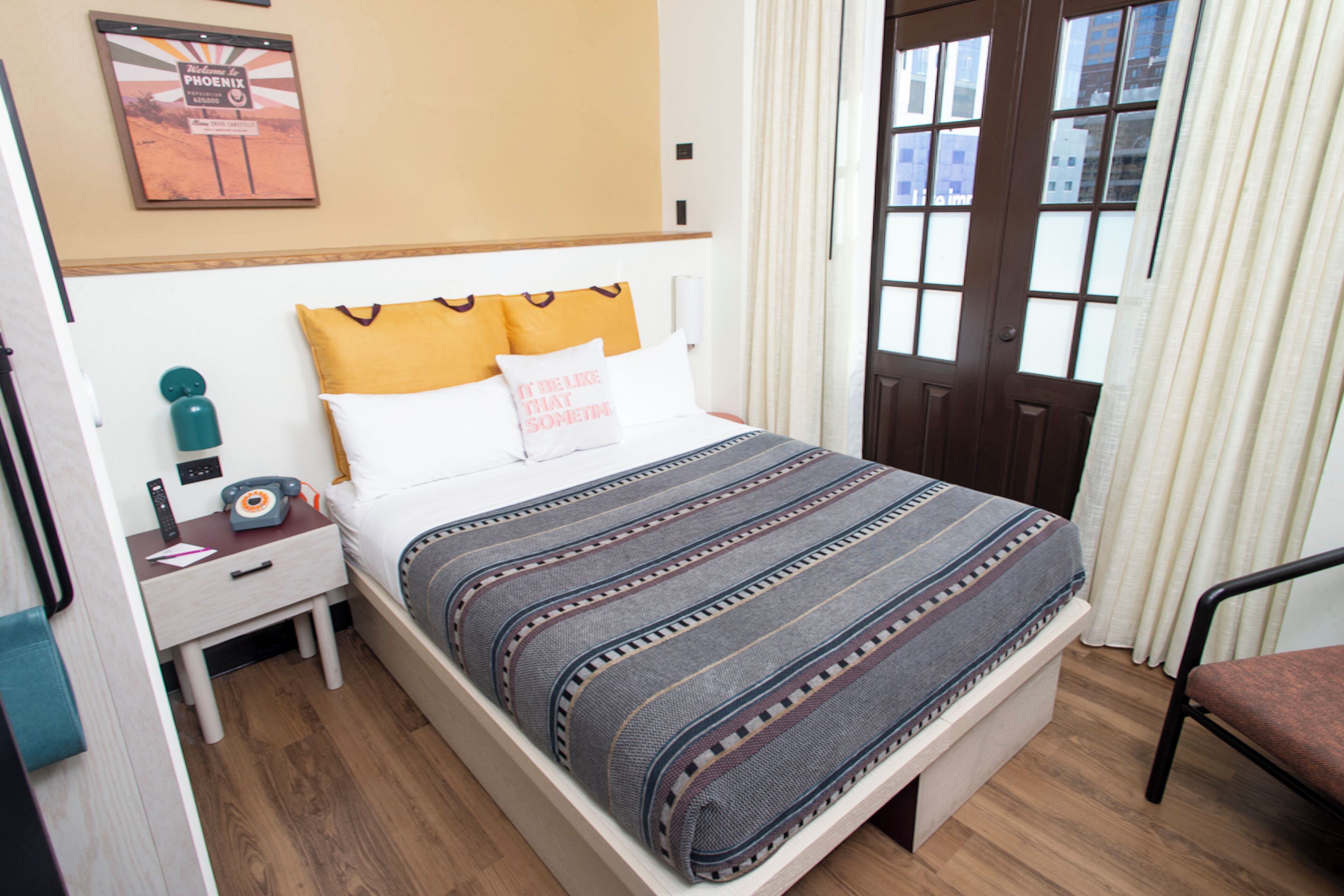 Une chambre d’hôtel bien rangée, avec un lit, une table de chevet, un téléphone et une affiche accrochée au mur.