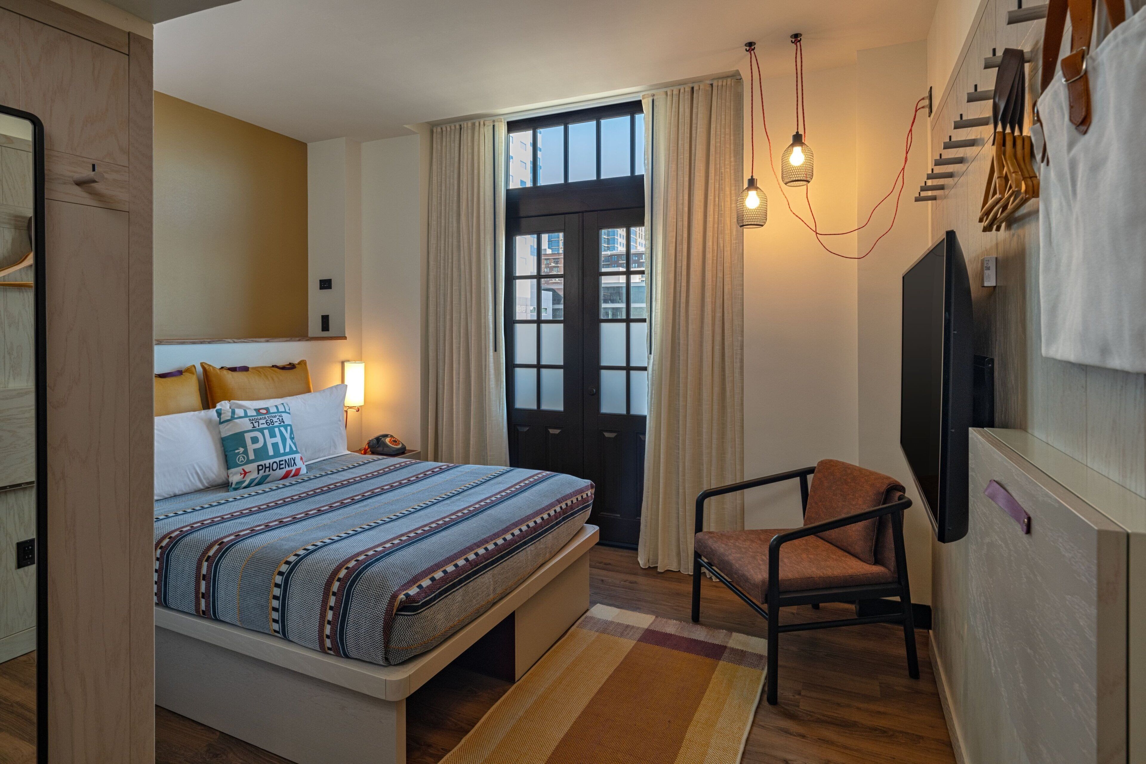 A hotel room with a bed, a chair, a TV, and a window with curtains.
