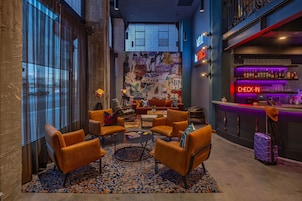 A modern lounge area with orange armchairs, a round coffee table, and a check-in counter with a neon sign.