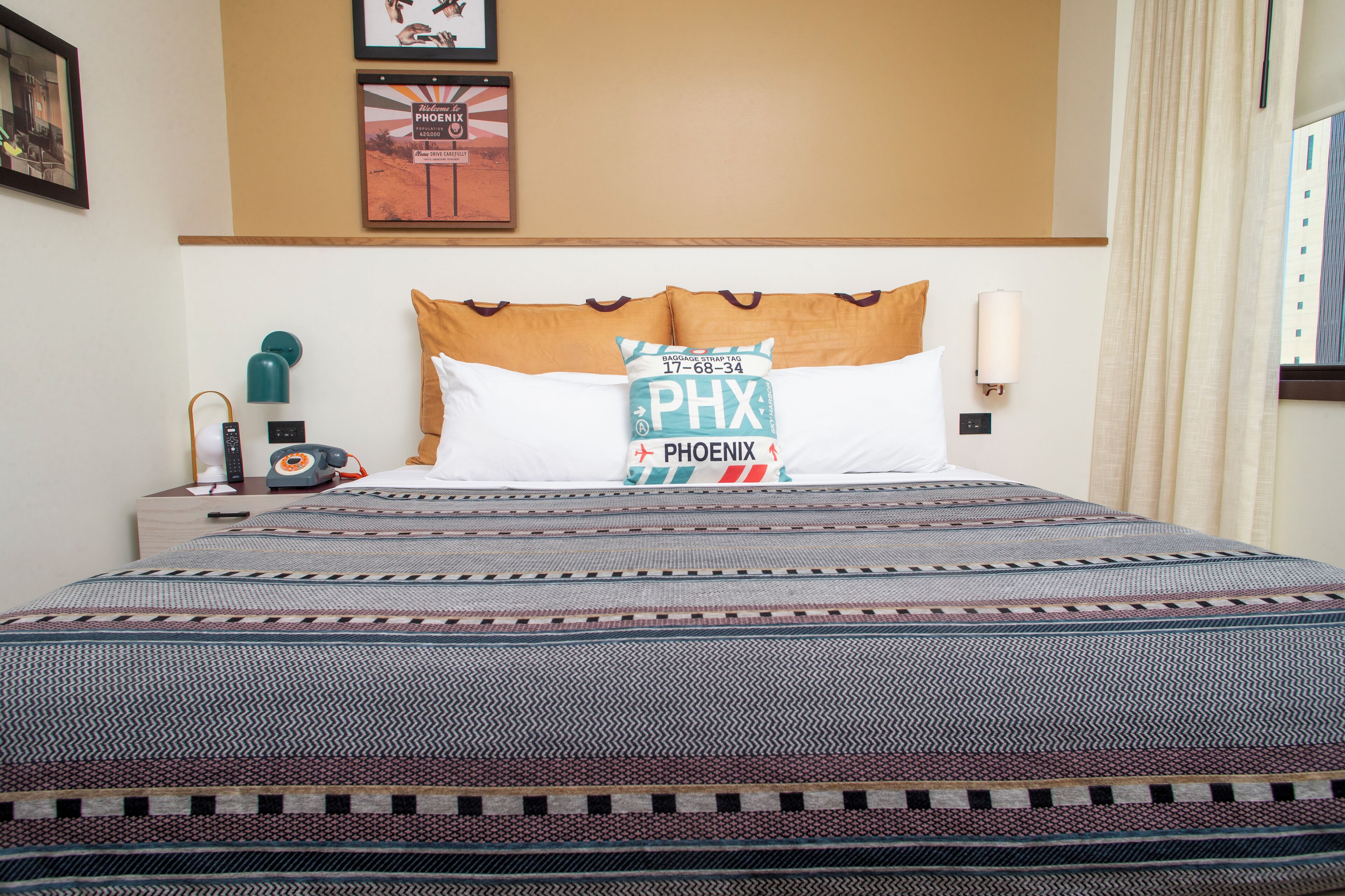 A hotel room with a bed, a nightstand with a lamp, a wall clock, and a framed picture.