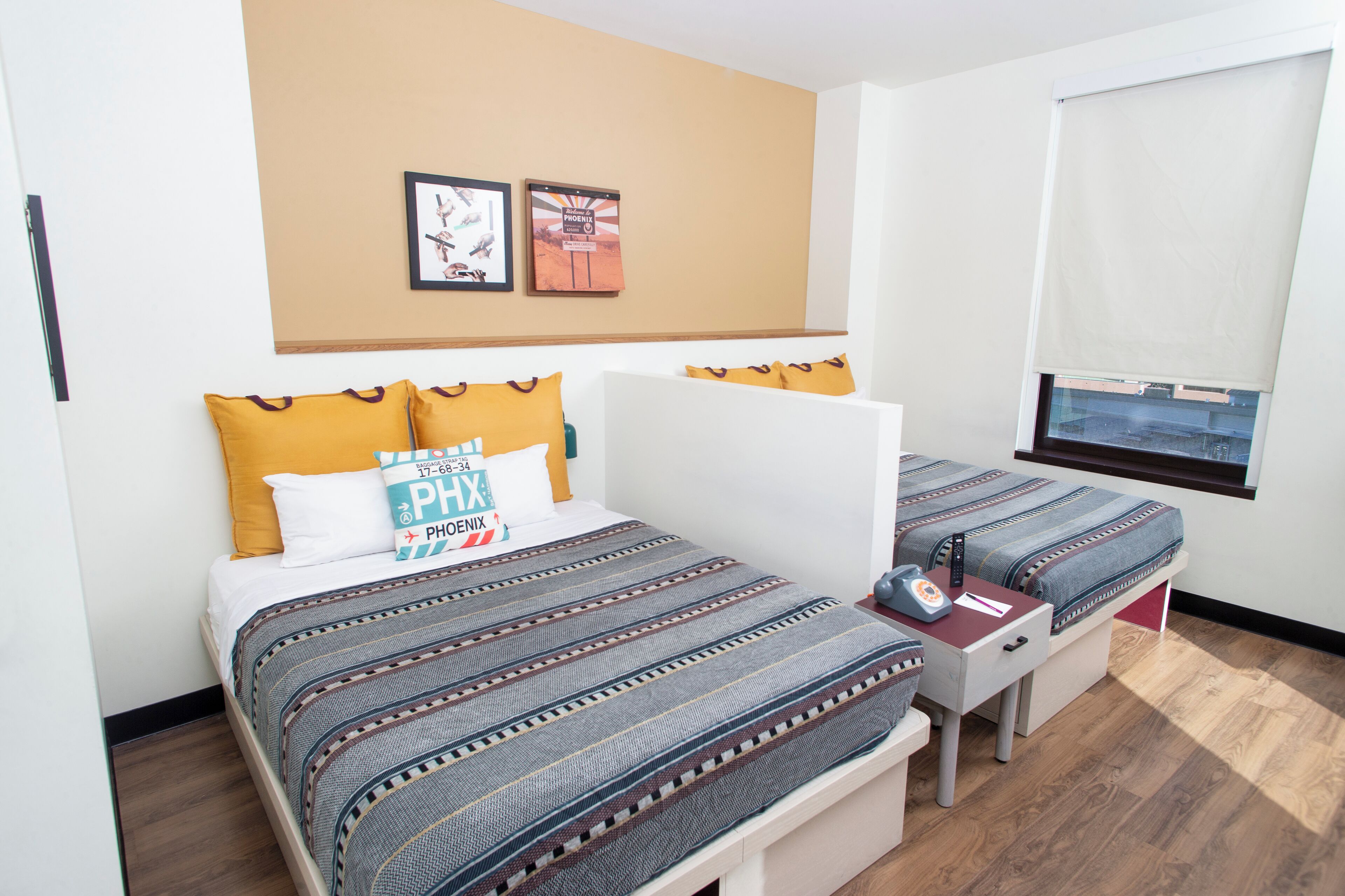 Habitación de hotel con dos camas, un escritorio, una silla, una ventana con vistas y una pared decorada con cuadros.