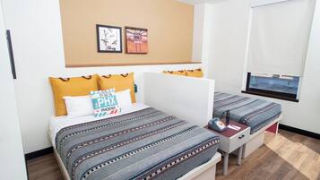 Habitación de hotel con dos camas, un escritorio, una silla, una ventana con vistas y una pared decorada con cuadros.
