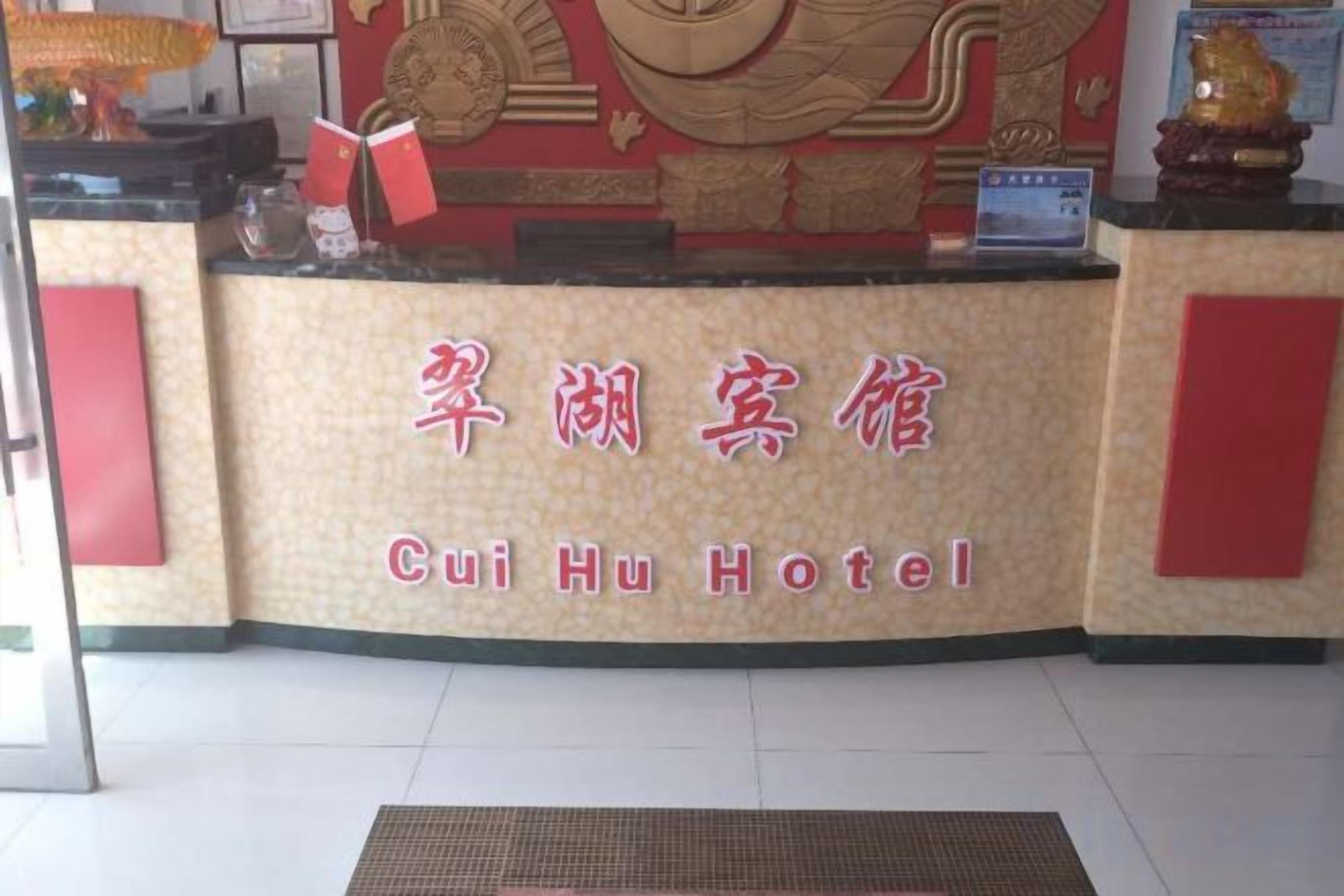 A hotel reception desk with a sign that reads 'Cui Hu Hotel' in both Chinese and English.