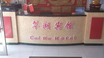 A hotel reception desk with a sign that reads 'Cui Hu Hotel' in both Chinese and English.
