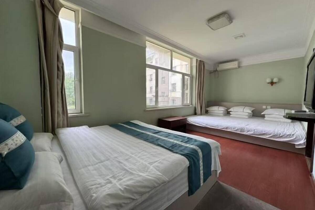 Une chambre d’hôtel avec deux lits, une fenêtre, une table de chevet et un climatiseur fixé au mur.