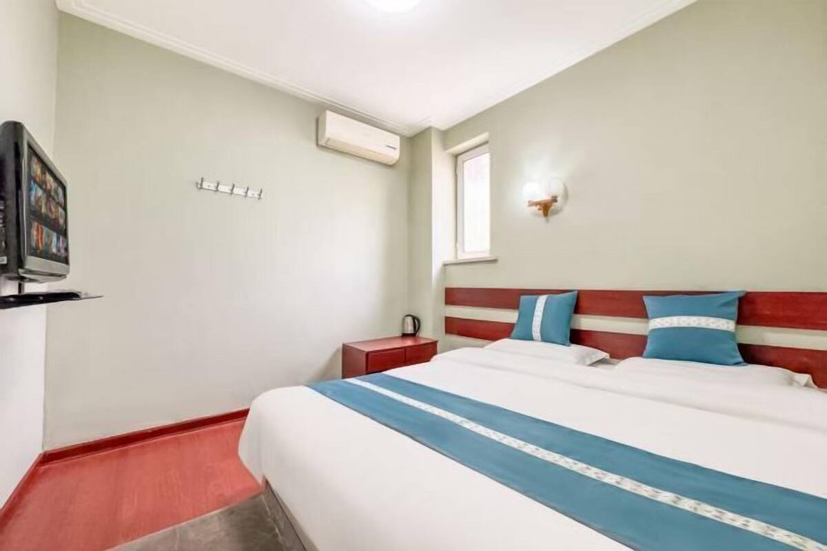 Une chambre d’hôtel avec un lit, une télévision, une fenêtre et un sol rouge.