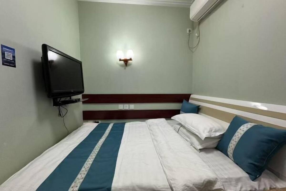 Une chambre d’hôtel avec un lit, un téléviseur à écran plat fixé au mur, un luminaire mural et un petit panneau accroché au mur.