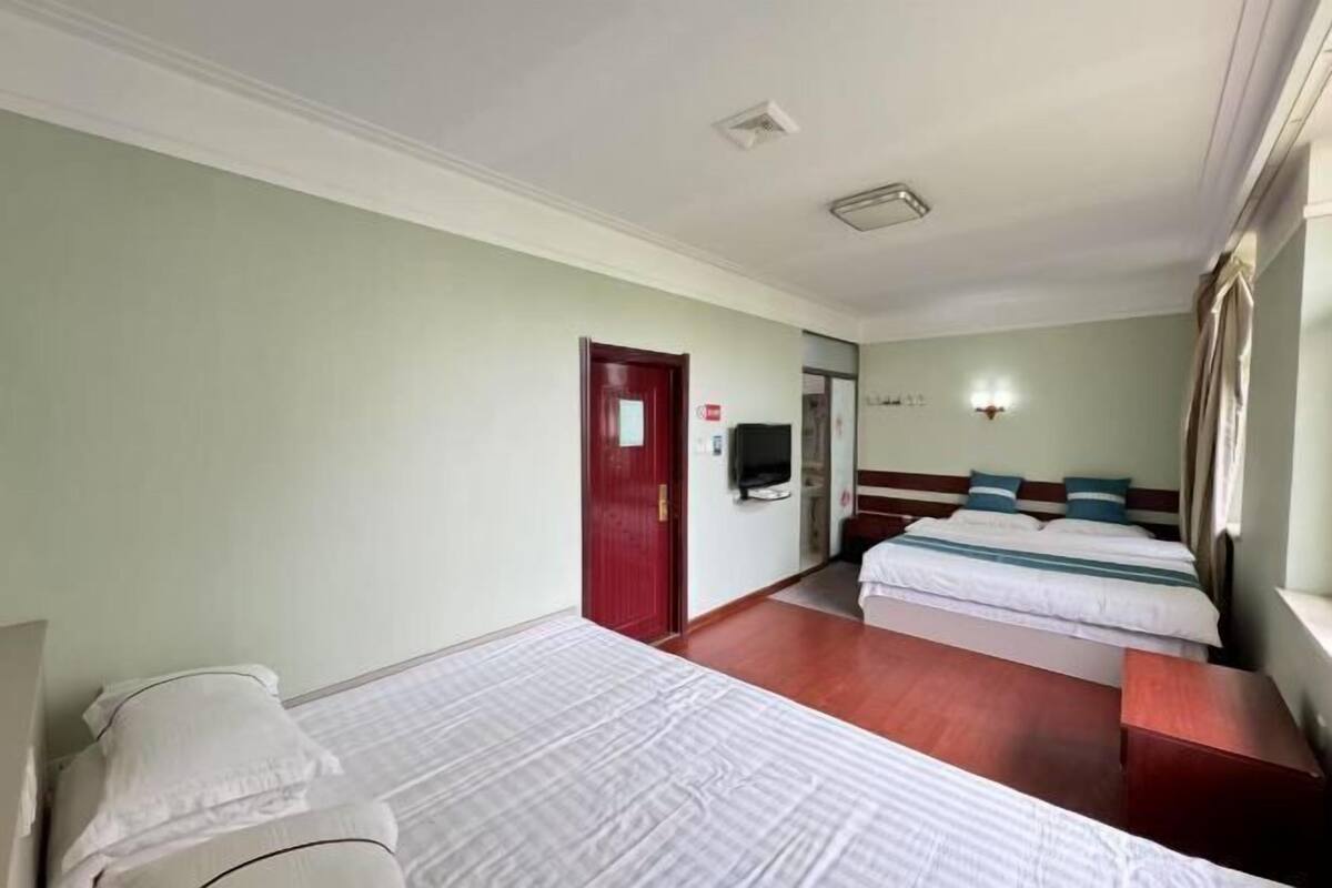 Une chambre d’hôtel avec deux lits, une porte rouge, un téléviseur et une fenêtre avec des rideaux.