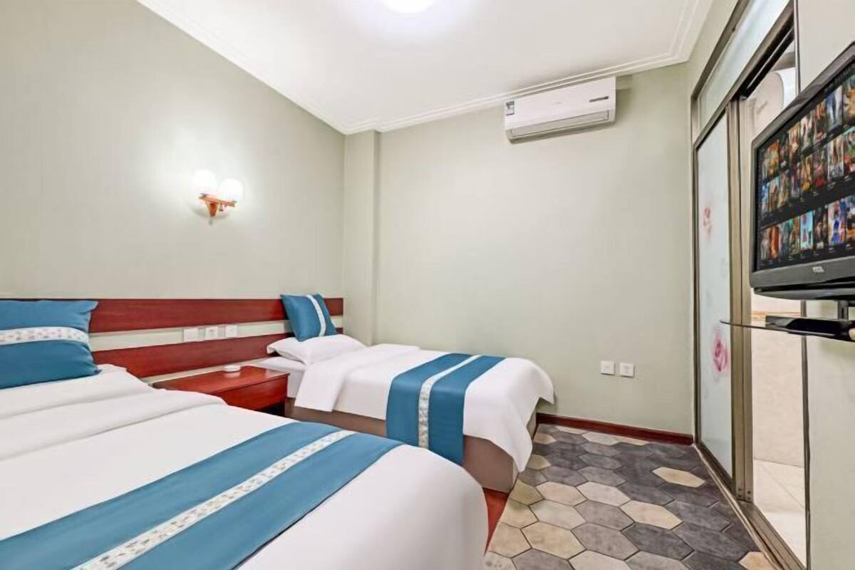 Une chambre d’hôtel avec deux lits, une télévision, un appareil de climatisation et un sol carrelé.