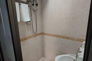 Un baño pequeño con azulejos, ducha, inodoro y perchero para toallas.