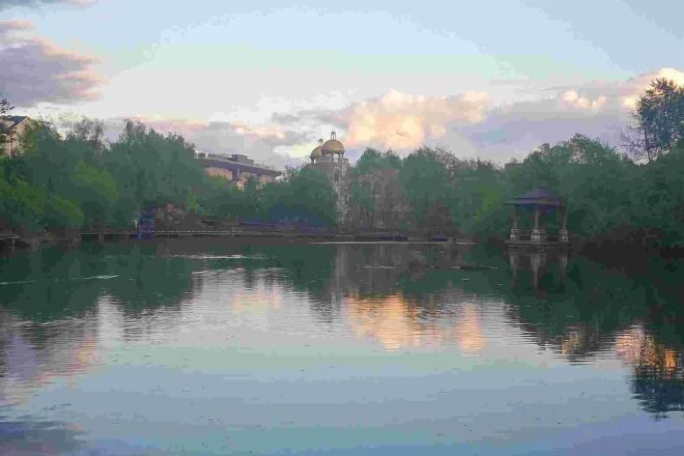 A calm lake with a gazebo and a pavilion in the distance.