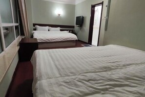 Habitación de hotel con dos camas, un televisor de pantalla plana montado en la pared y una ventana con cortinas.