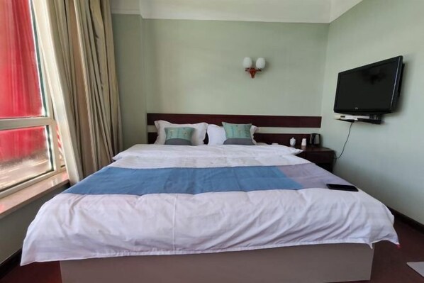 Habitación de hotel con una cama, un televisor montado en la pared y un ventanal con cortinas.