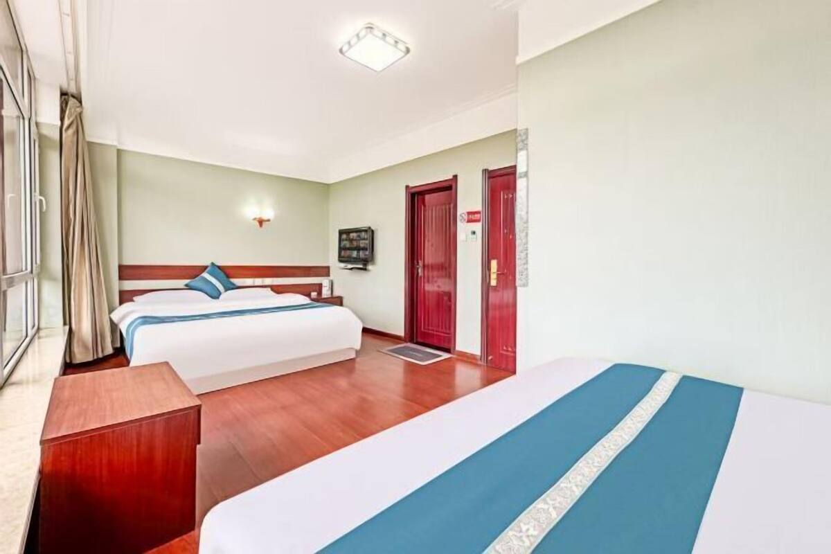 Une chambre d’hôtel avec deux lits, un plancher en bois, une porte rouge et un luminaire fixé au mur.