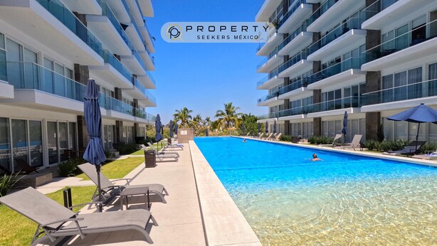 A modern hotel with a swimming pool, sun loungers, and a clear blue sky.