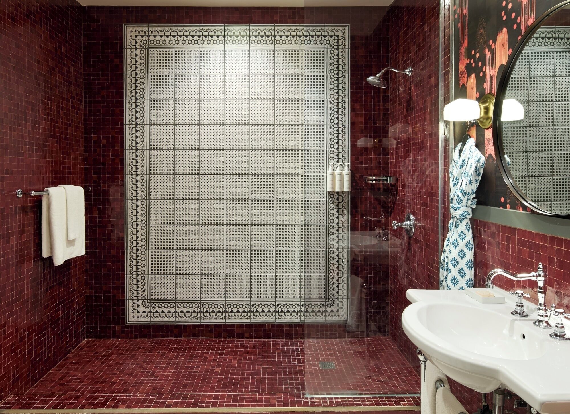 Un baño con una puerta grande de diseño, un lavamanos blanco y un espejo con marco redondo.