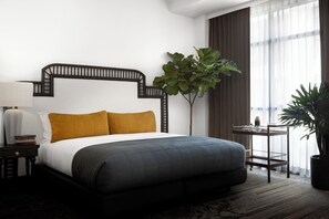 Habitación de hotel moderna con una cama grande, una mesita de noche, una pequeña mesa y una planta en maceta.