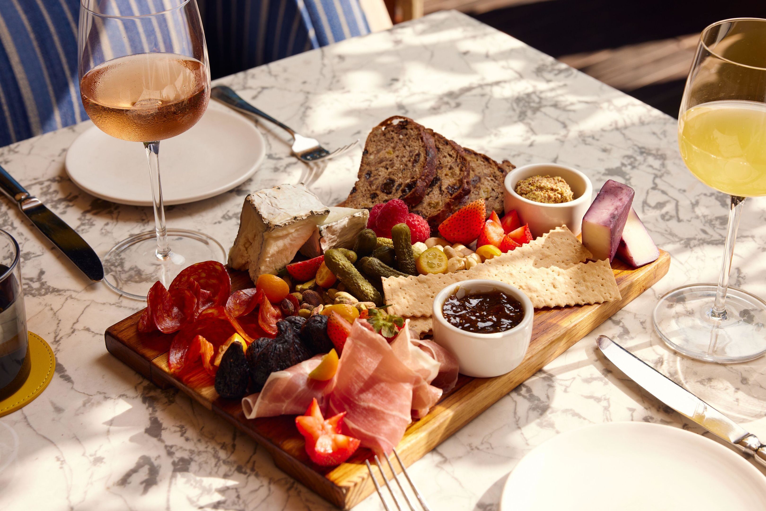 A marble table with a charcuterie board, wine glasses, and cutlery.
